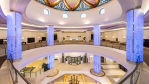 Een ruime hotellobby met een centraal atrium, diverse zithoeken en een decoratief plafond.