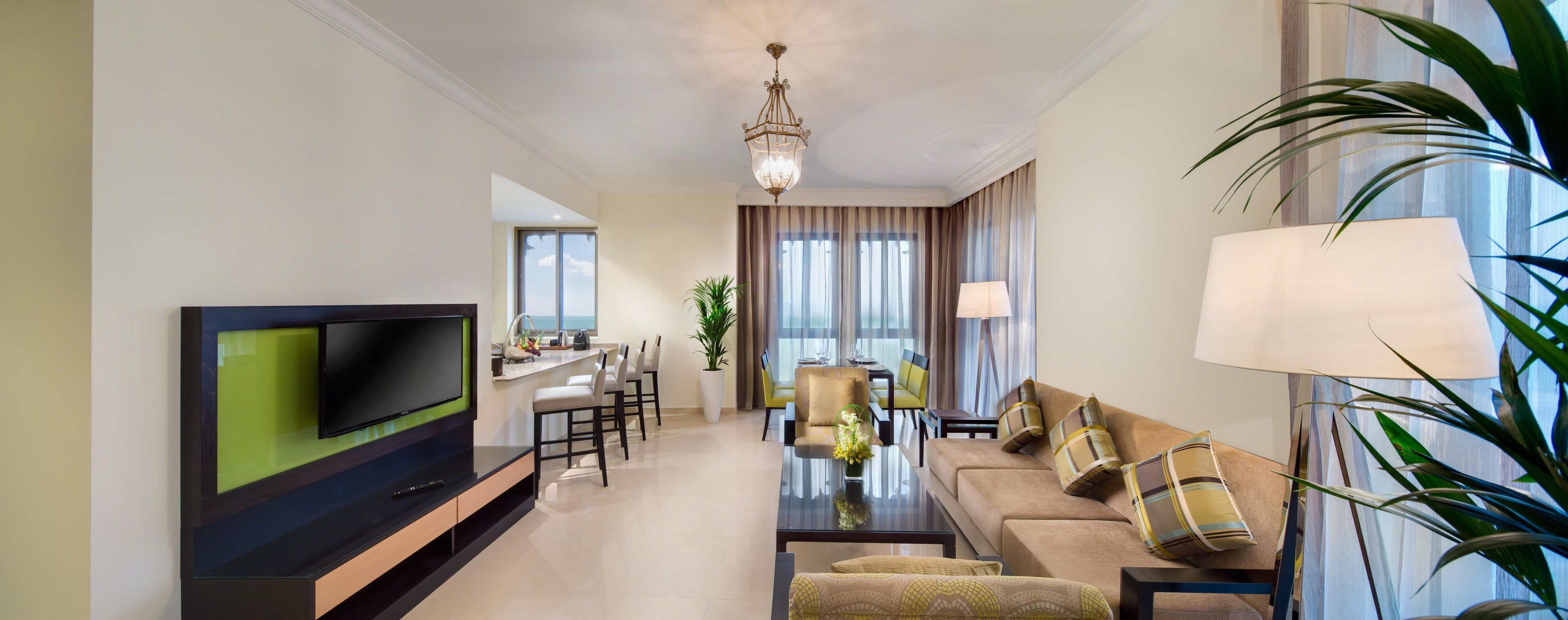 A modern living room with a flat-screen TV, a dining area with chairs and a table, and a sofa with decorative pillows.