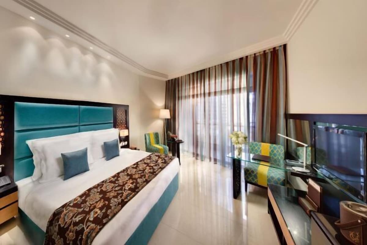 A hotel room with a large bed, a TV, a glass coffee table, and a view of the outdoors.