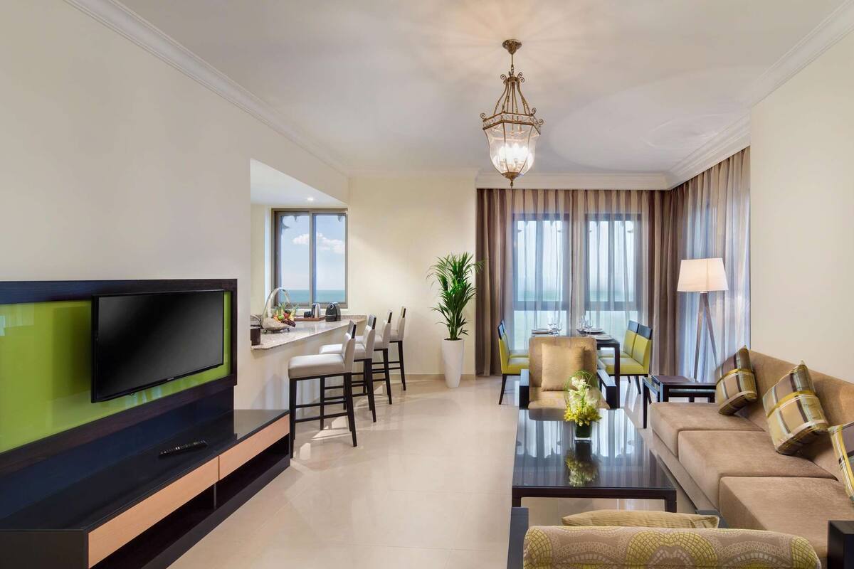Una sala de estar moderna con televisor de pantalla plana, un comedor con mesa y sillas, y un sofá con almohadones decorativos.