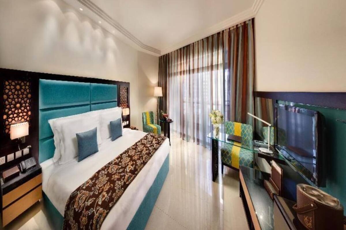 Habitación de hotel con una cama grande, una mesa de vidrio, un televisor y vistas al exterior.