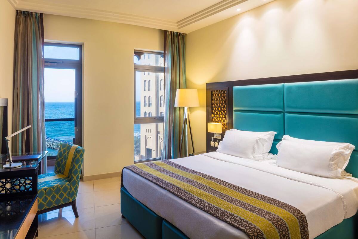 Habitación de hotel con una cama grande, una silla, un escritorio y vista al mar.