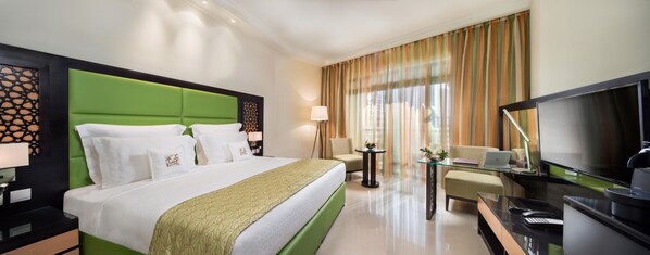 Una habitación de hotel con una cama grande, un televisor, un escritorio con una computadora portátil y una silla.
