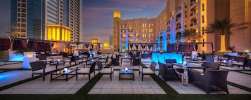 An outdoor lounge area with seating and a bar, surrounded by buildings.