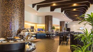 Zona de buffet con piso a cuadros, una isla central con comida y un pilar grande con mosaicos.