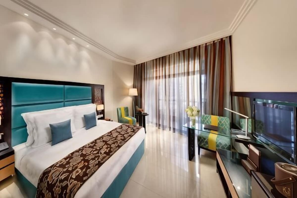 A hotel room with a large bed, a TV, a glass table, and a view of the outdoors.