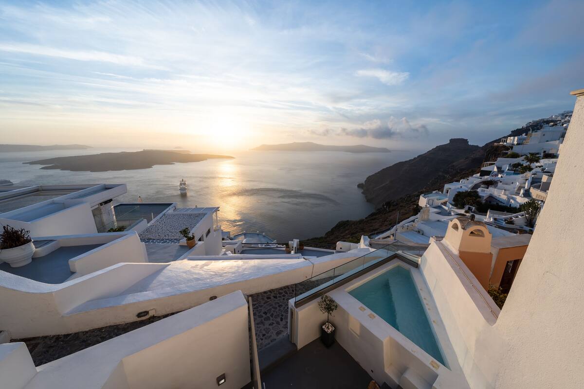 Vista costera con piscina, edificios blancos y un atardecer sobre el mar.