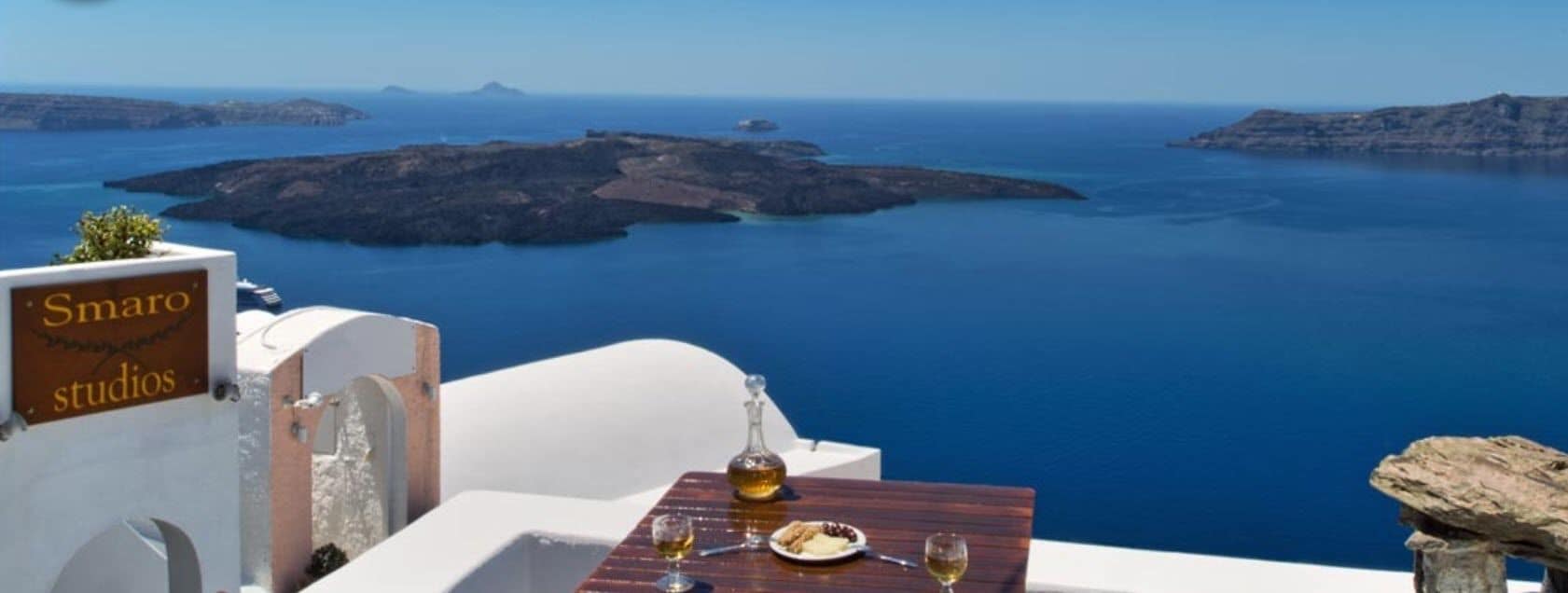 A table with a bottle and glasses, overlooking a scenic view of the sea and islands.