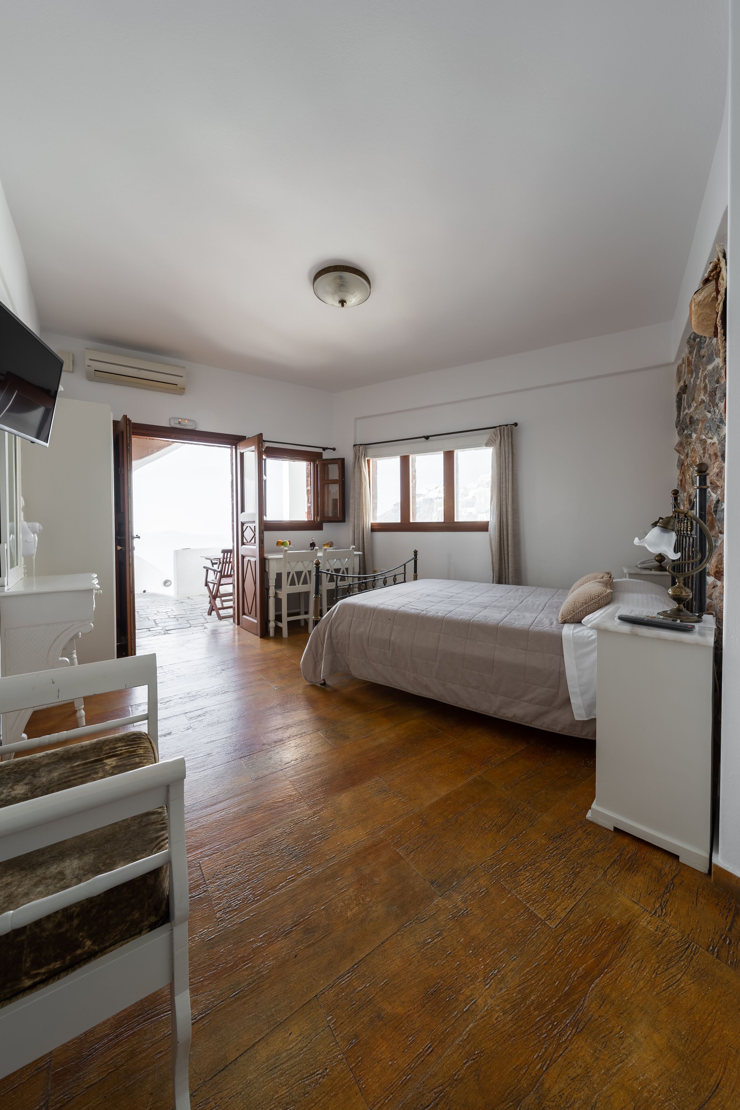 A bedroom with a bed, a desk, and a chair. There is a window with curtains and a view of the outside.