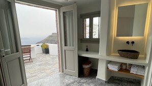 A modern bathroom with a marble floor, a large mirror, and a view of the sea through an open door. - Smaro Studios (Santorini)