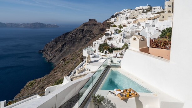 A seaside hotel with a pool, white architecture, and a view of the sea and a rocky cliff. - Smaro Studios (Santorini)
