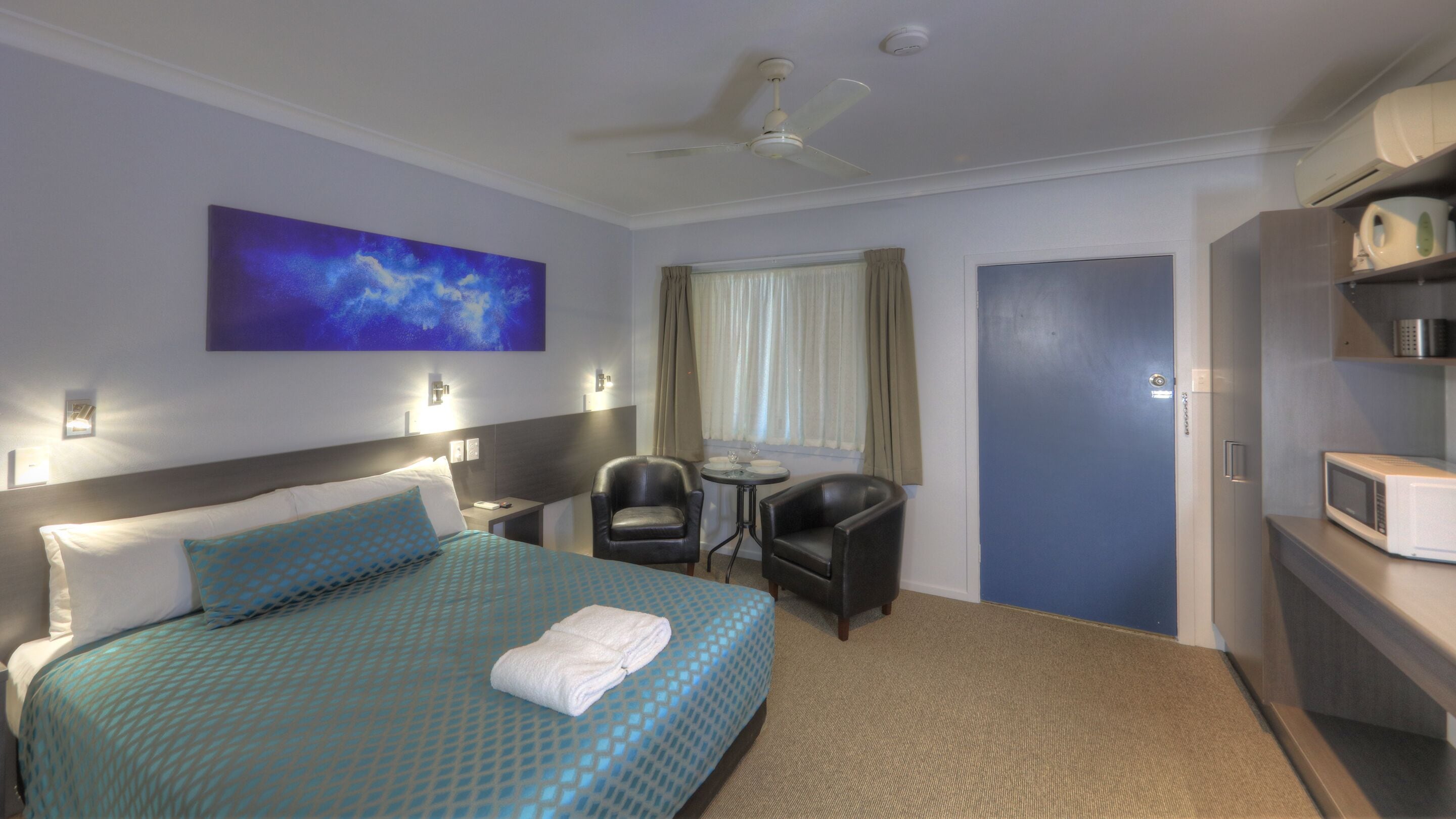 A hotel room with a bed, a desk, a chair, a microwave, and a door.