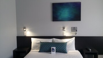 Una habitación de hotel con cama, mesita de noche, control remoto y cartel en la pared.