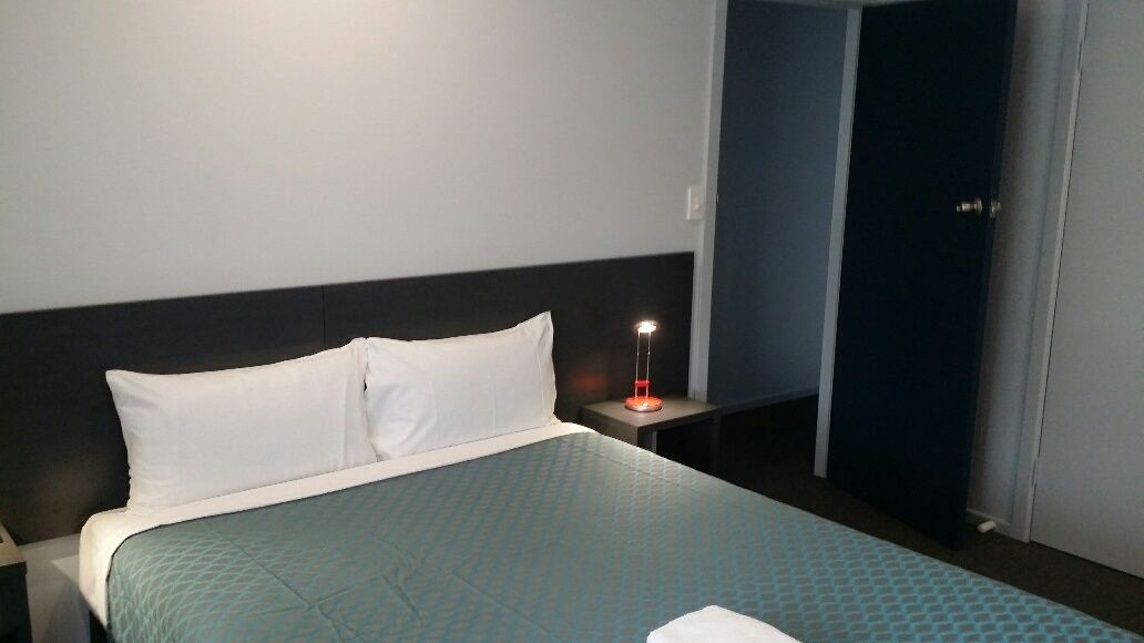 A hotel room with a bed, a bedside table with a lamp, and a door.