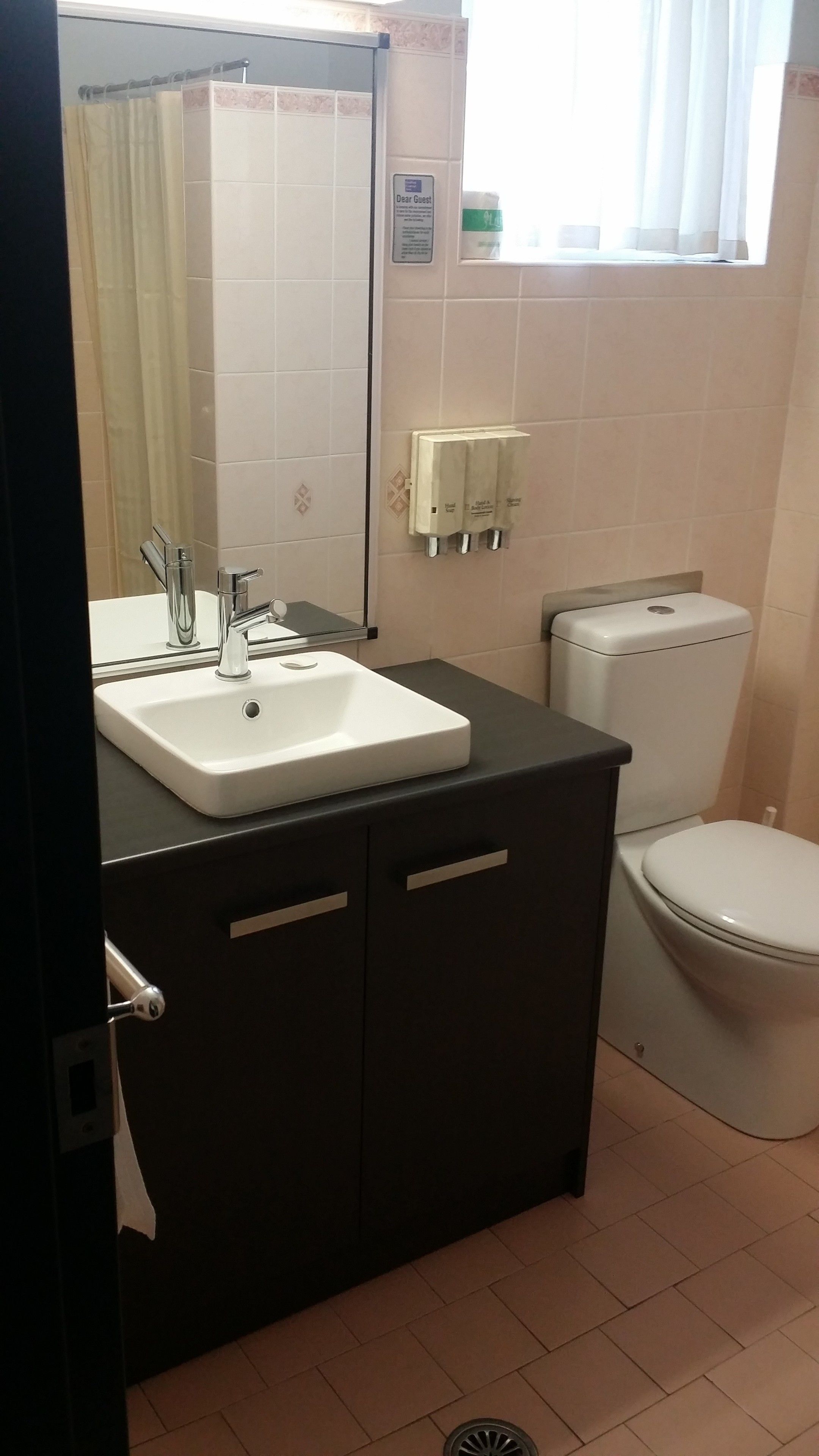 A bathroom with a white sink, dark cabinets, a toilet, and a mirror.
