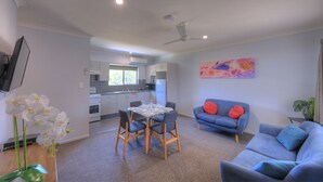 A modern kitchen with white cabinets, a dining area with a table set for four, a blue sofa with red cushions, and a ceiling fan. - Grafton Central Motel (Grafton)