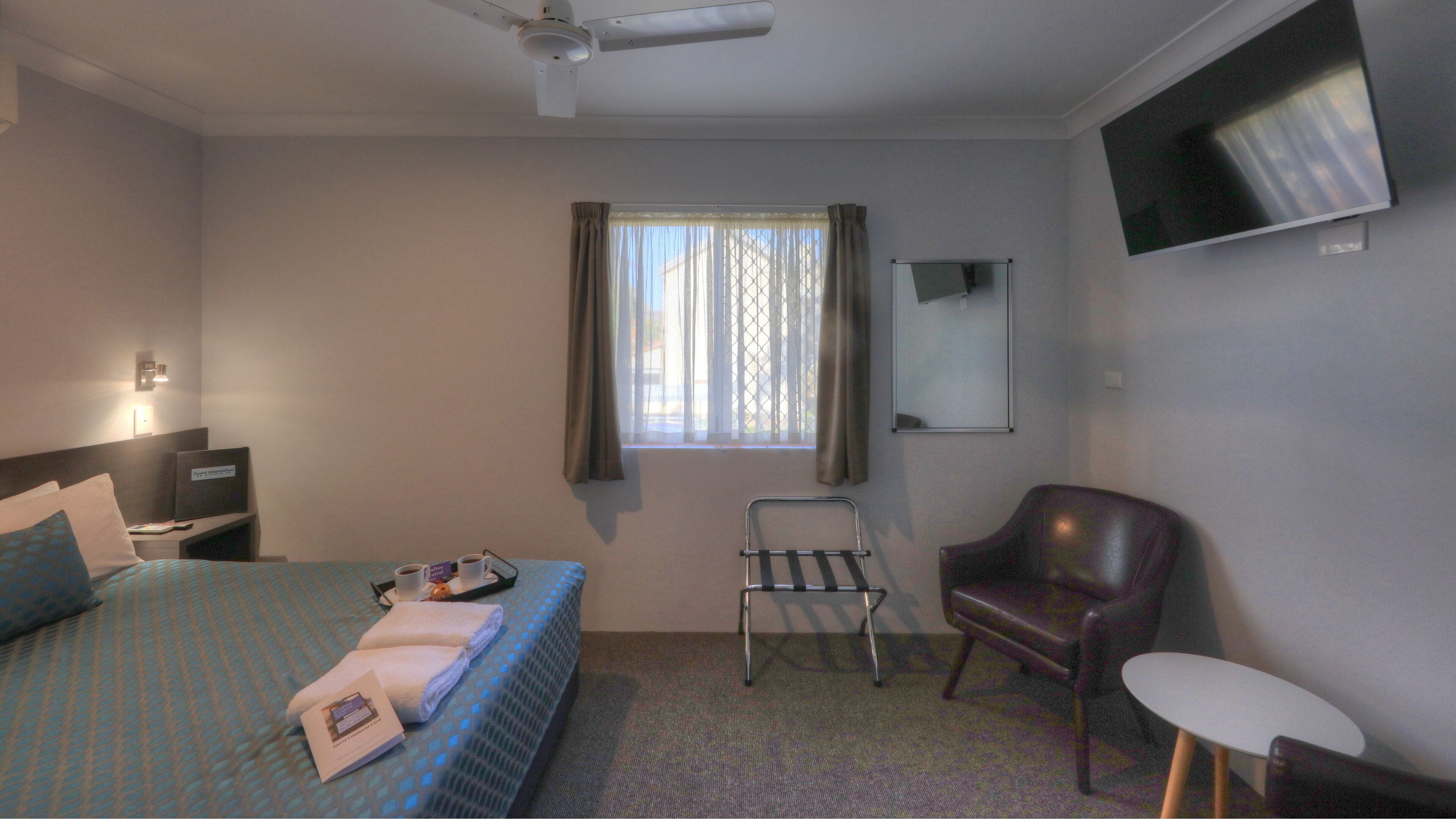 Een hotelkamer met een bed, een stoel, een tafeltje, een televisie en een raam met gordijnen.