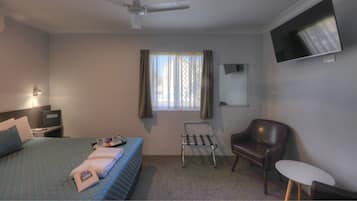 Een hotelkamer met een bed, een stoel, een tafeltje, een televisie en een raam met gordijnen.