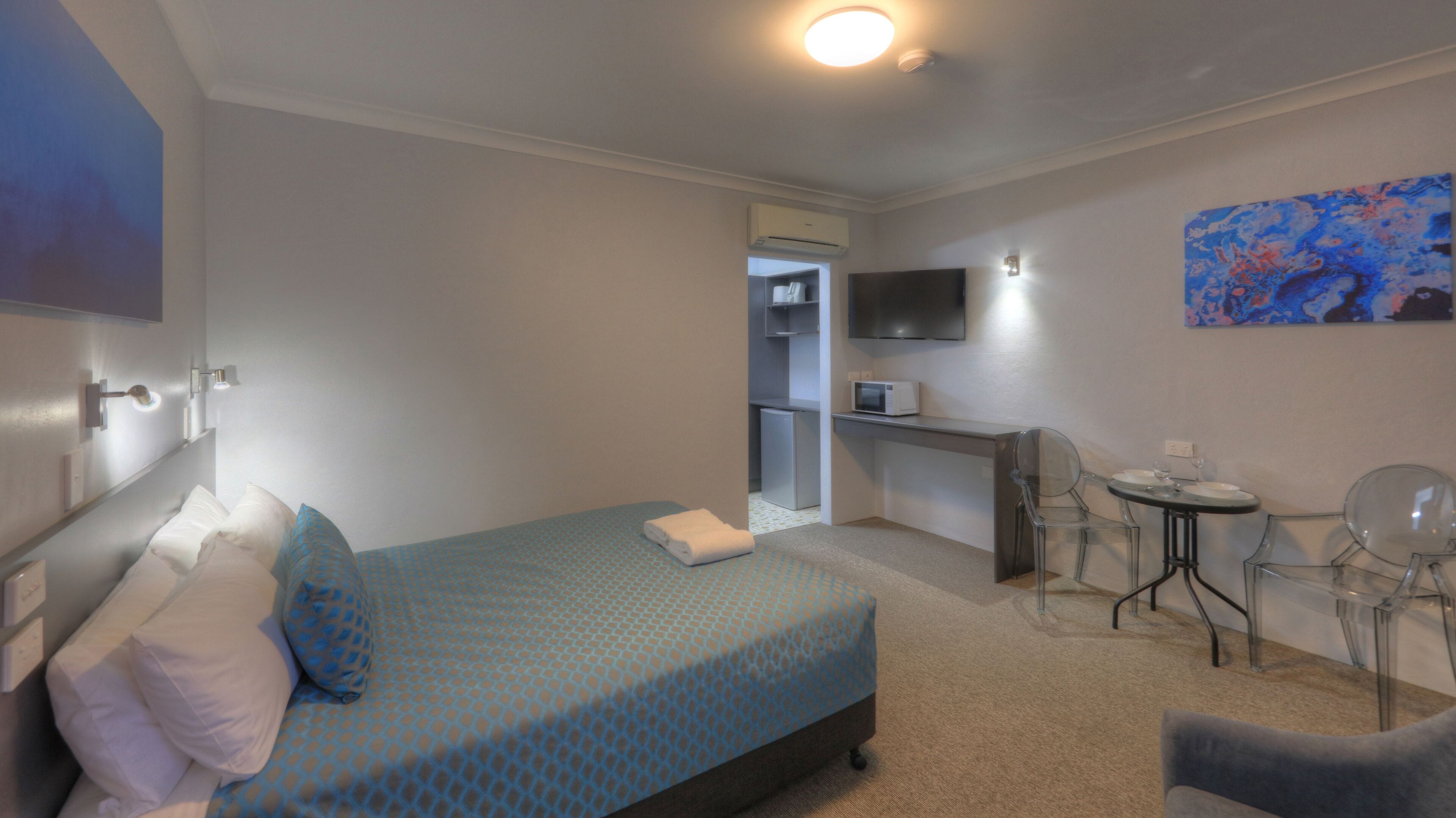 A hotel room with a bed, a desk, a chair, a TV, and a painting on the wall.