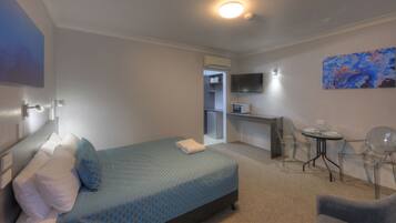 A hotel room with a bed, a desk, a chair, a TV, and a painting on the wall.