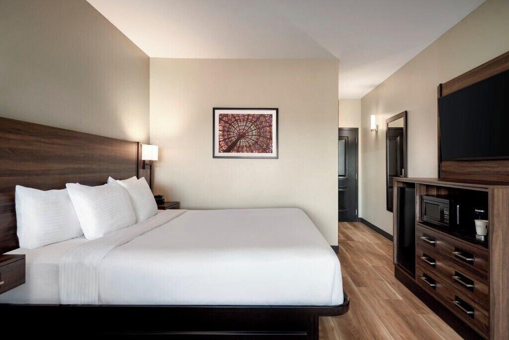 Une chambre d’hôtel avec un grand lit, une œuvre d’art accrochée au mur, un téléviseur et une armoire en bois.