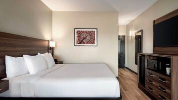 A hotel room with a large bed, a wall-mounted artwork, a television, and a wooden cabinet.