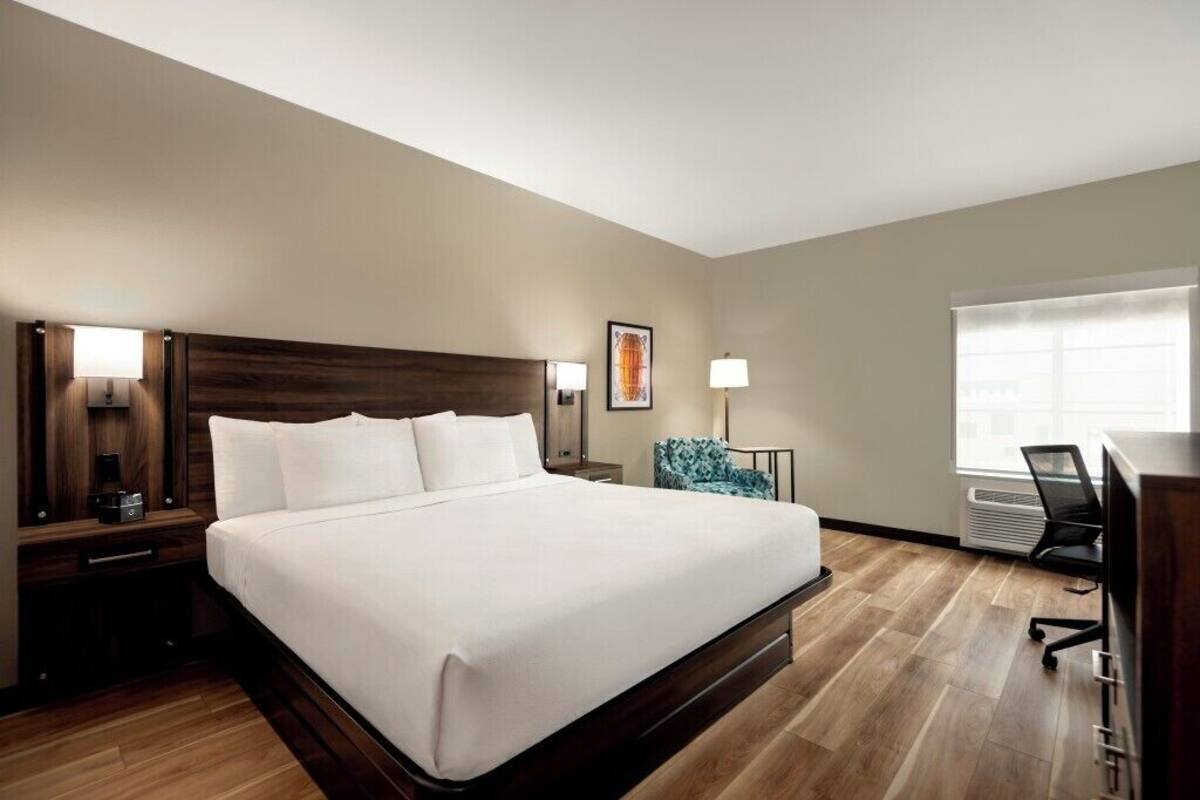 A hotel room with a large bed, bedside tables with lamps, a chair, a desk, and a window.