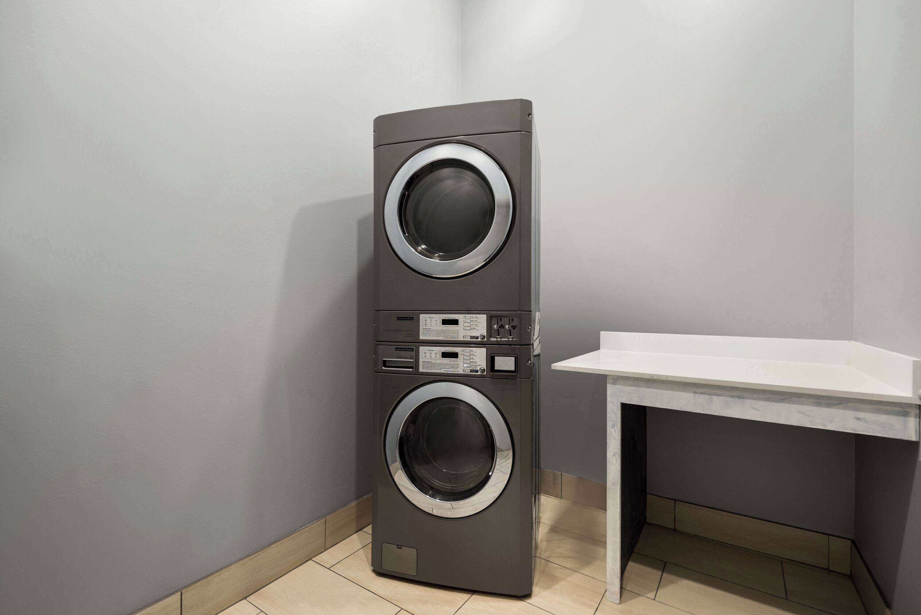 A compact, modern laundry room with a tall, gray wall-mounted washer and dryer, a small white sink, and a tiled floor.