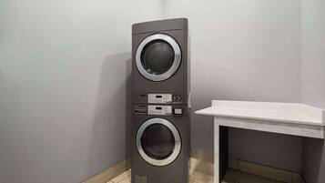 A compact, modern laundry room with a tall, gray wall-mounted washer and dryer, a small white sink, and a tiled floor.