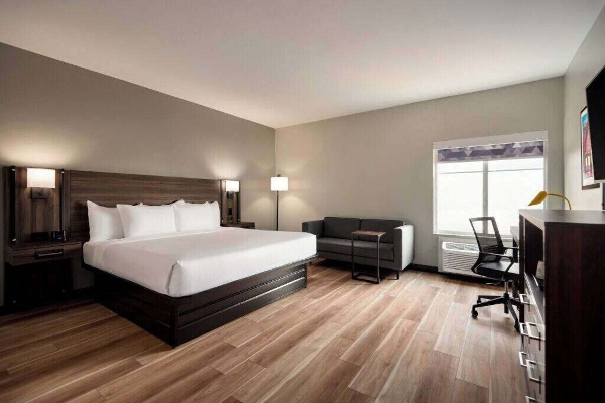 A modern hotel room with a large bed, a sofa, a desk, and a window.