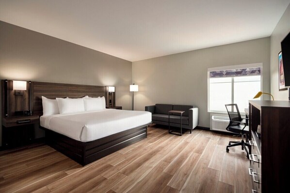 Ein modernes Hotelzimmer mit einem großen Bett, einer Couch, einem Schreibtisch und einem Fenster.