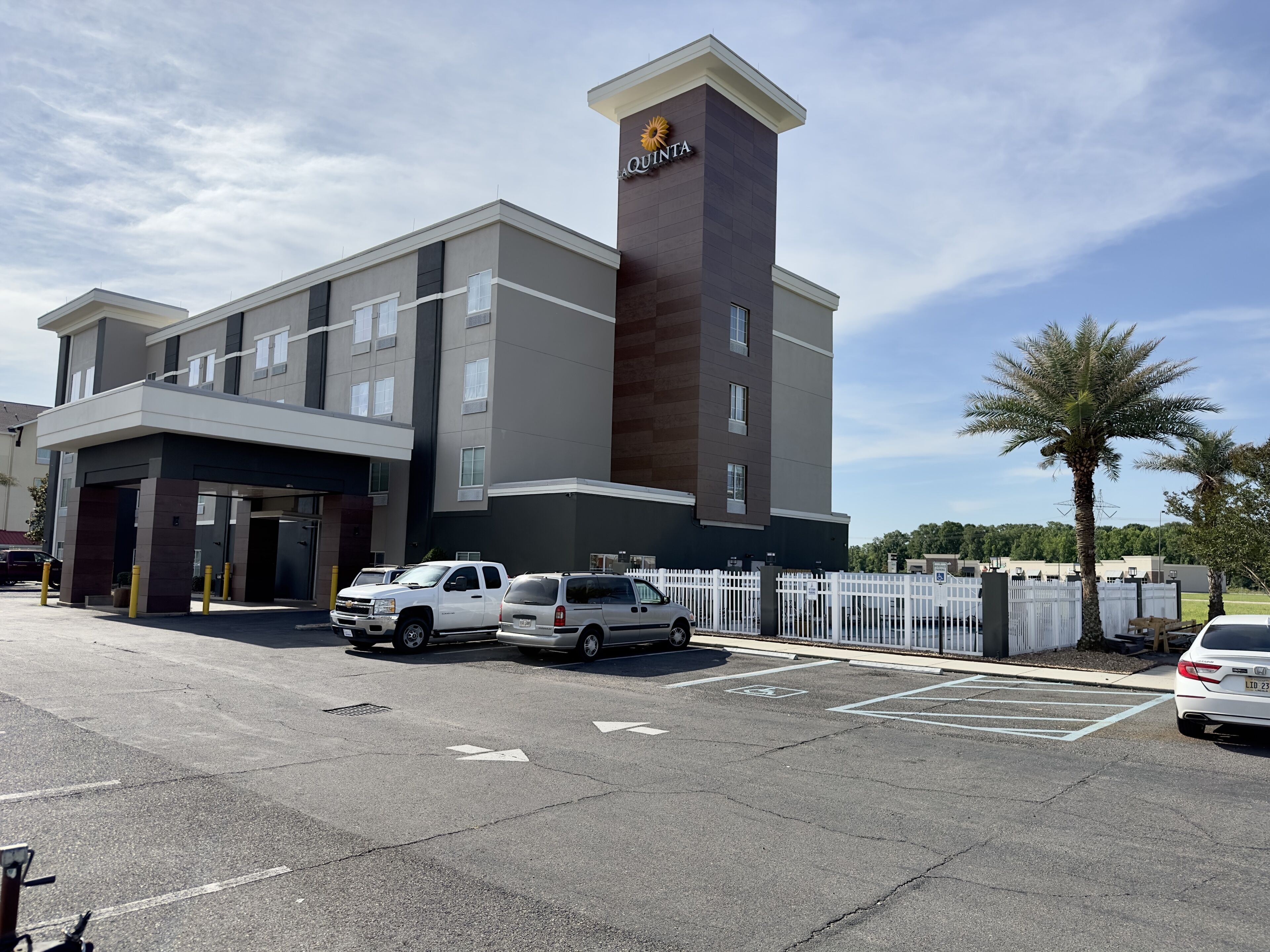 A modern hotel with a prominent tower, multiple parking spaces, and a gated entrance.