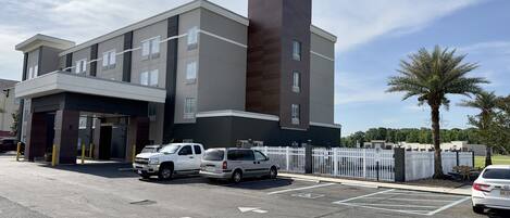 A modern hotel with a prominent tower, multiple parking spaces, and a gated entrance.