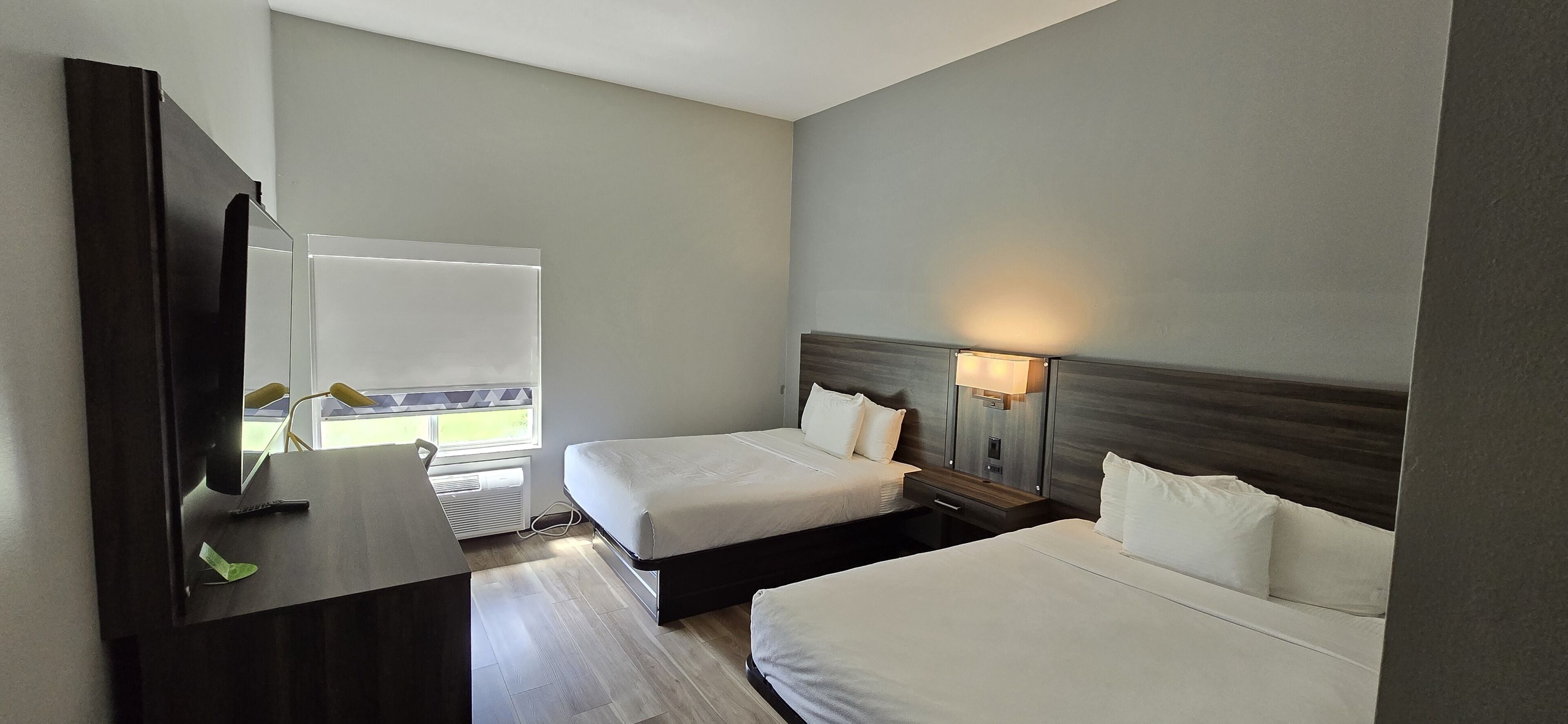 A hotel room with two beds, a desk, a TV, and a window with blinds.