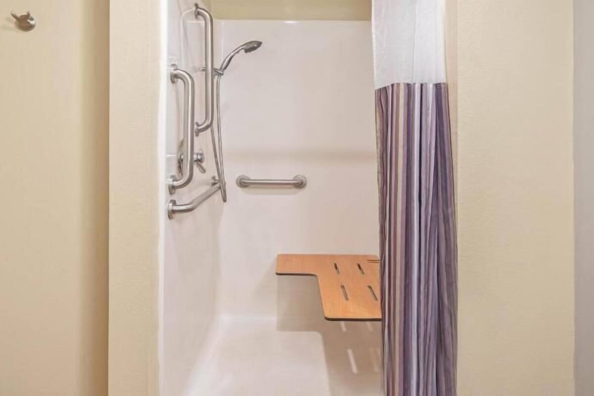 A shower with a grab bar, a wooden shelf, and a striped curtain.