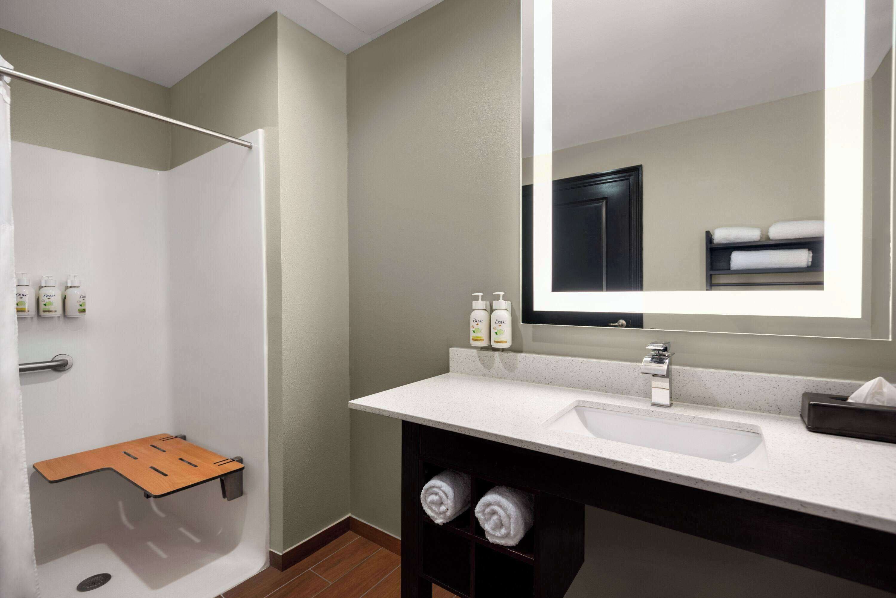A modern bathroom with a shower, a sink, and a mirror. There are towels and toiletries on the counter.
