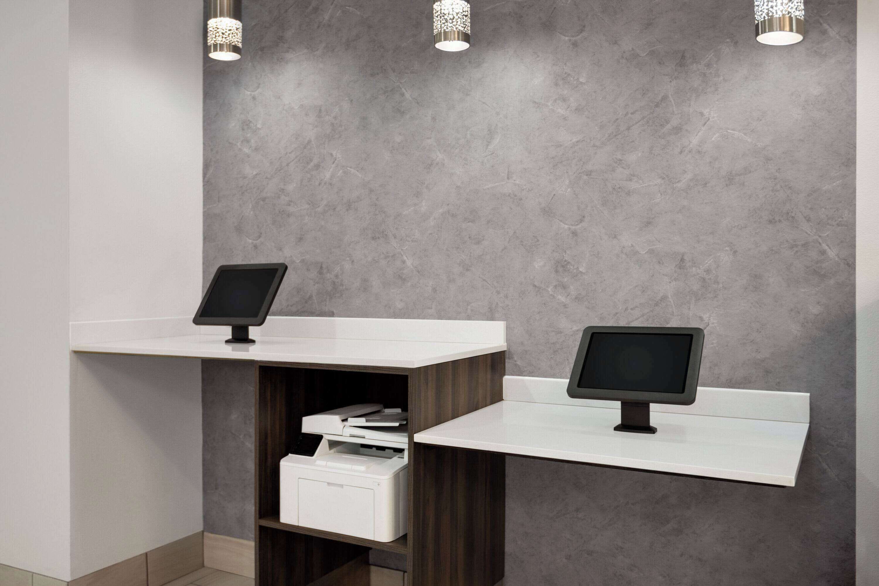 A reception area with two white reception desks, each with a monitor, against a grey textured wall.