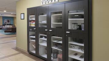 A LENDING LOCKER with multiple compartments for storage, located in a hallway with a tiled floor and a seating area in the background.