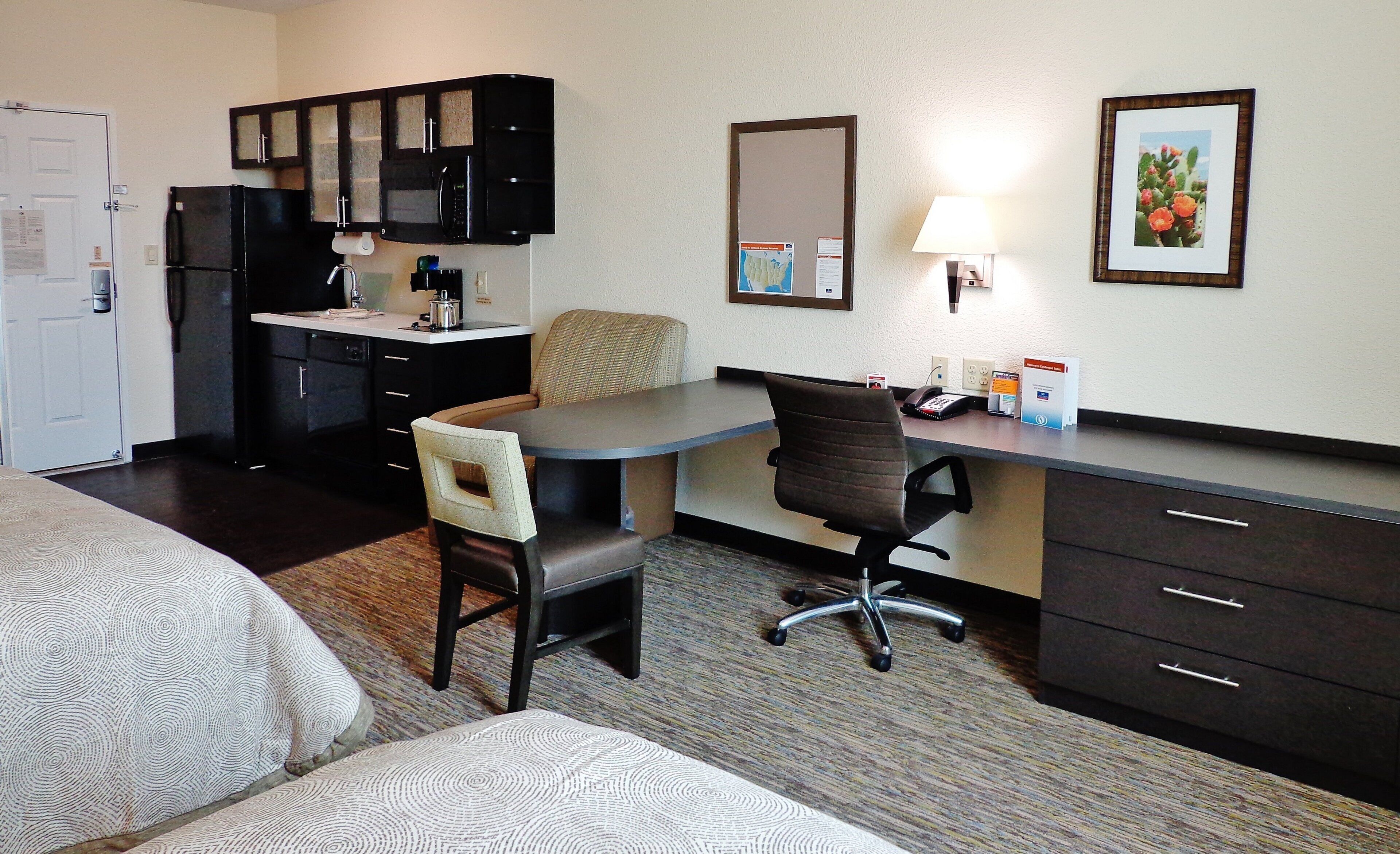 A hotel room with a kitchenette, a dining area, a desk with a chair, and a bed.