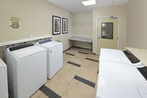 A laundry room with two front-loading washers, a bench, and a door leading to another room. - Candlewood Suites Odessa by IHG (Odessa)