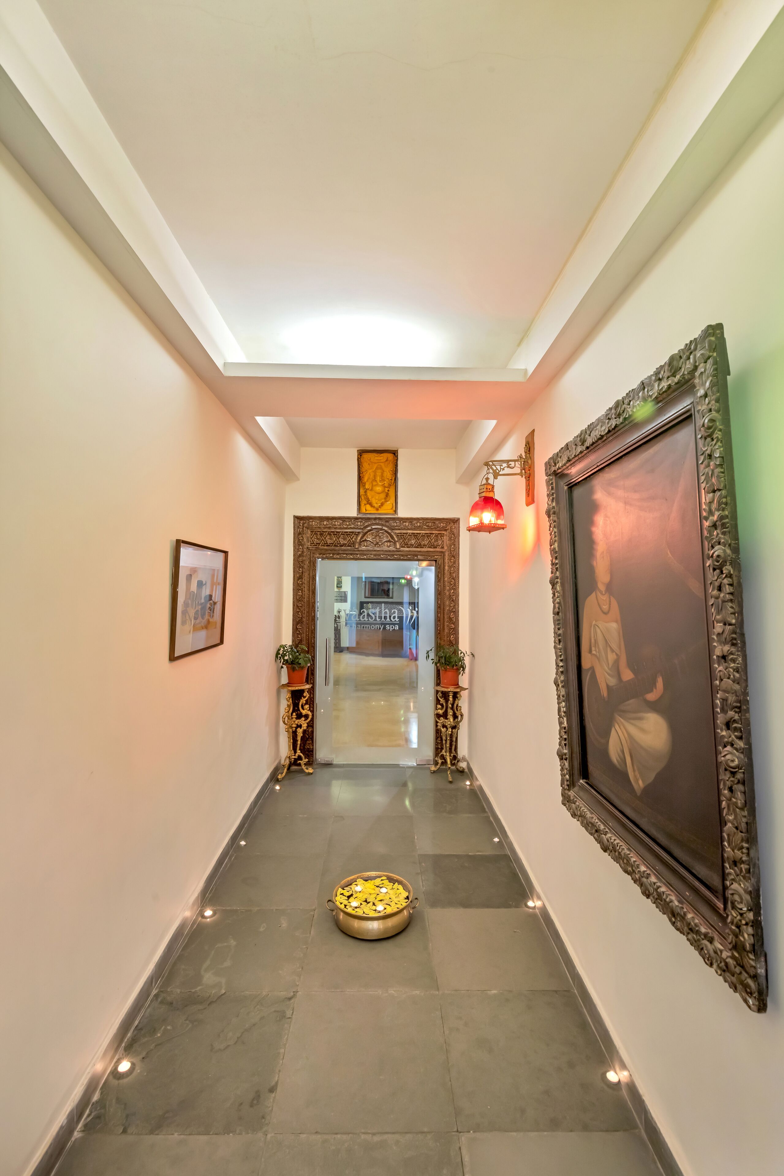 A hallway with a framed picture, a potted plant, and a decorative bowl on the floor.