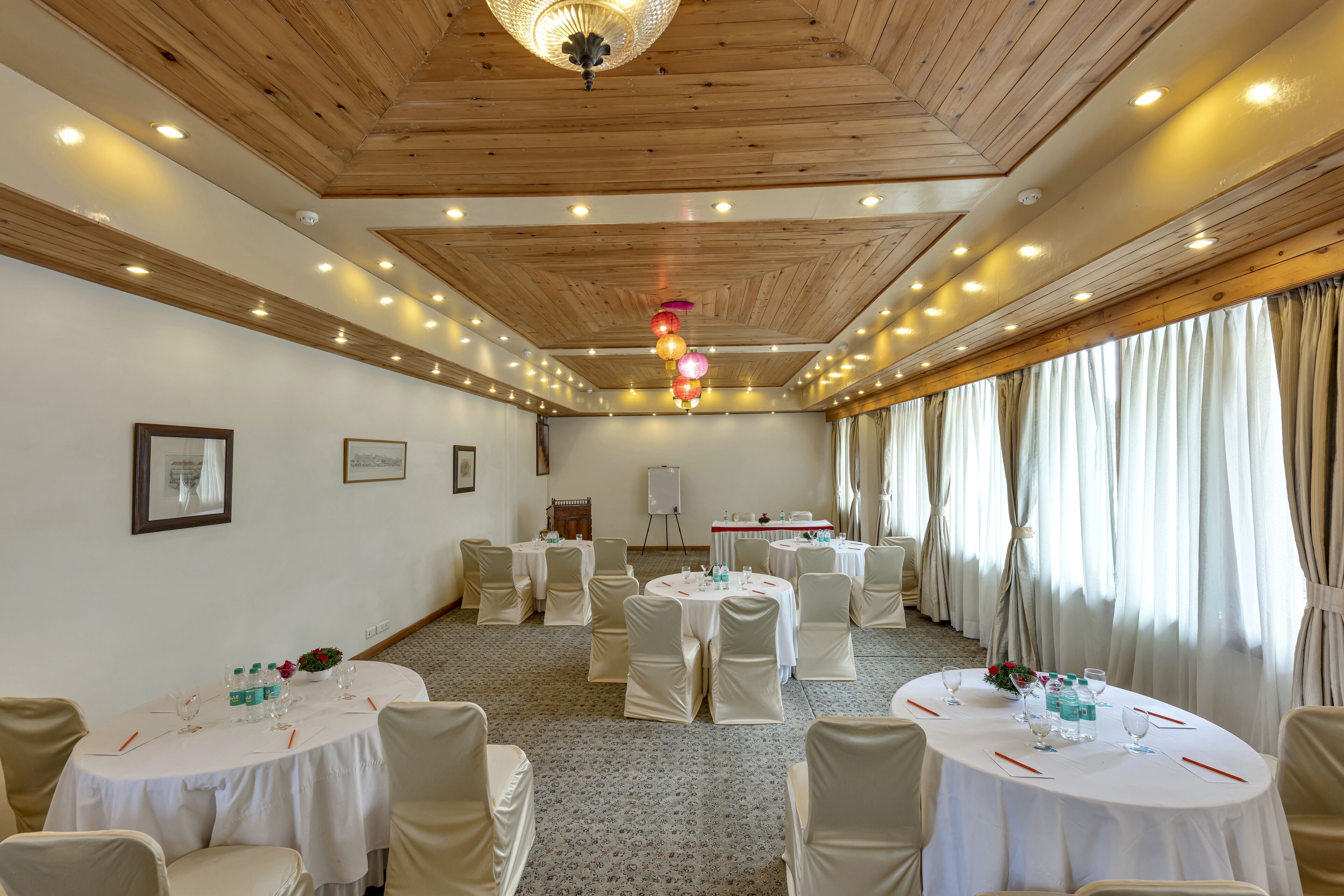 Un salón de conferencias con mesas redondas, manteles blancos y sillas color beige.