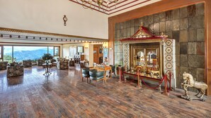 A spacious lobby with a grand chandelier, a decorative altar, and a view of the mountains through large windows. - Club Mahindra Mashobra (Shimla)