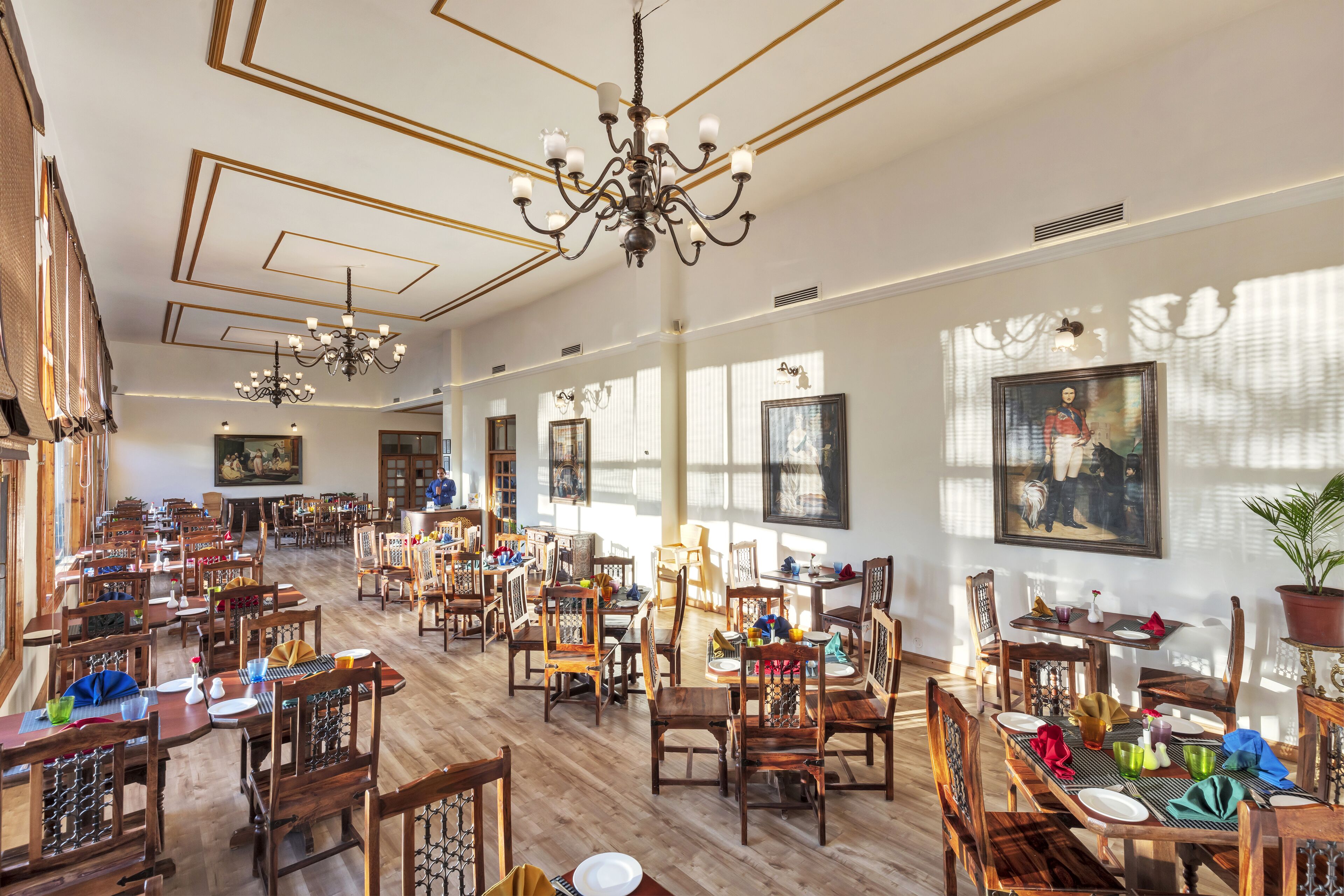 A spacious dining area with wooden tables and chairs, chandeliers, and framed artwork on the walls.