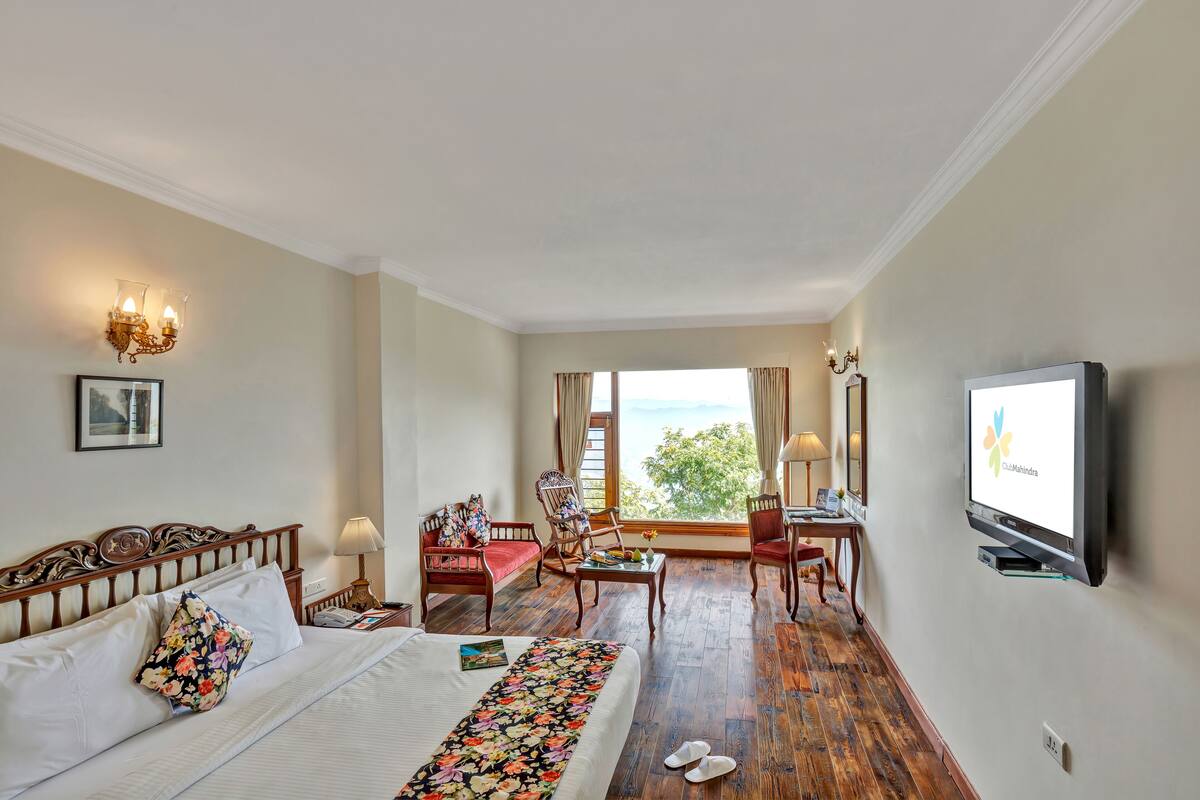 A hotel room with a bed, a desk, a chair, a TV, and a view of the outdoors.