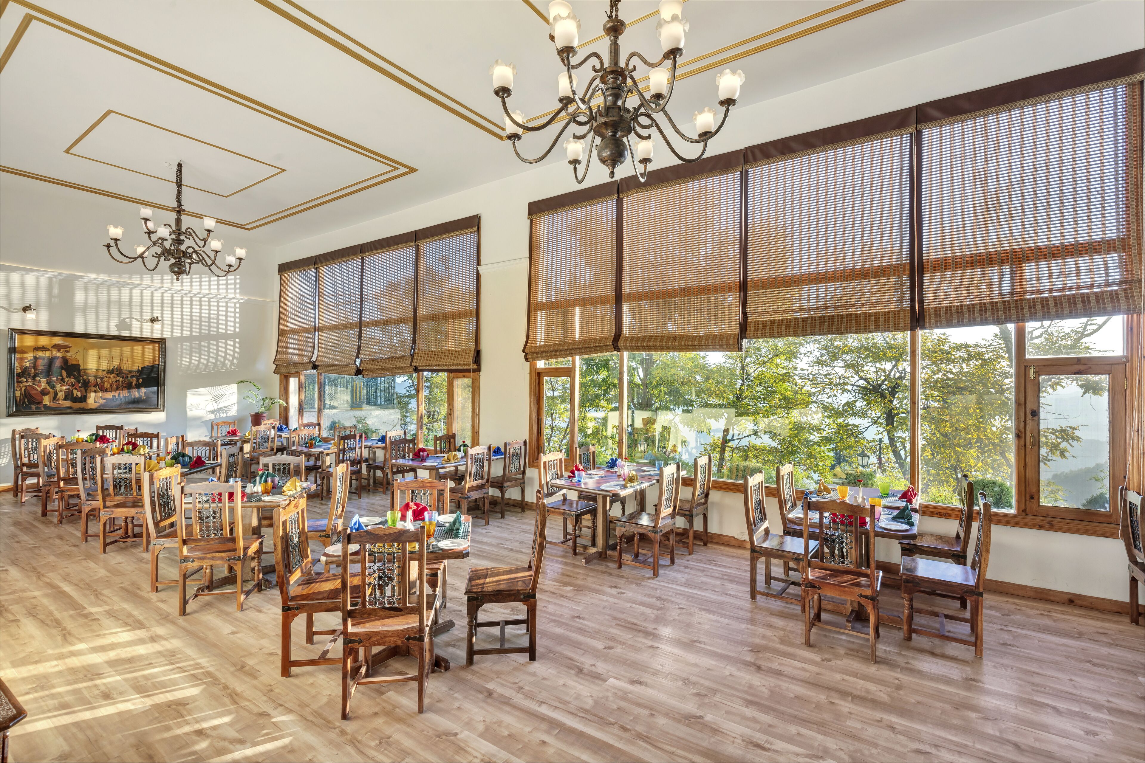 A spacious dining area with wooden tables and chairs, large windows with bamboo shades, and a chandelier.