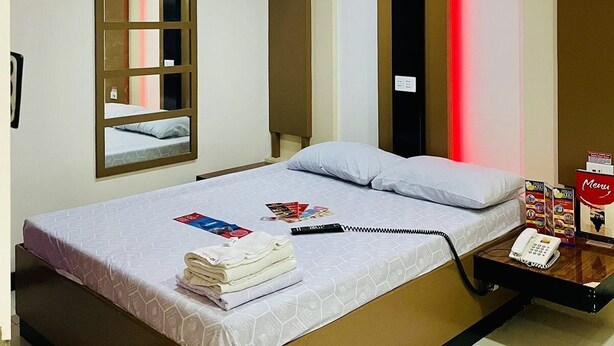 A hotel room with a bed, a bedside table with a phone, a mirror, and a window with blinds. - Hotel Sogo Dau (Mabalacat City)