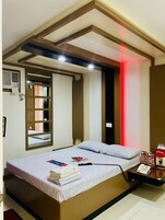 A hotel room with a bed, a bedside table with a phone, a mirror, and a window with blinds.