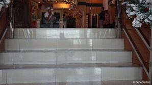 A set of white tiled stairs with a metal handrail, leading to a lobby area with a Christmas wreath and a poster. - Hotel Sogo Dau (Mabalacat City)