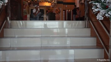 A set of white tiled stairs with a metal handrail, leading to a lobby area with a Christmas wreath and a poster.